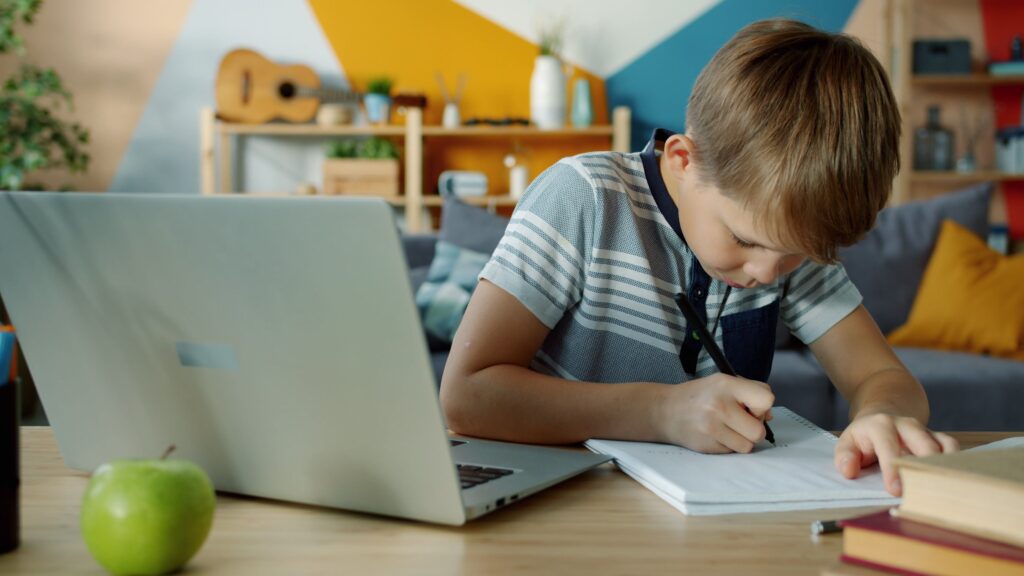 a child is studying at a desk with a laptop and a notebook