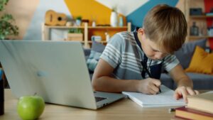 a child is studying at a desk with a laptop and a notebook
