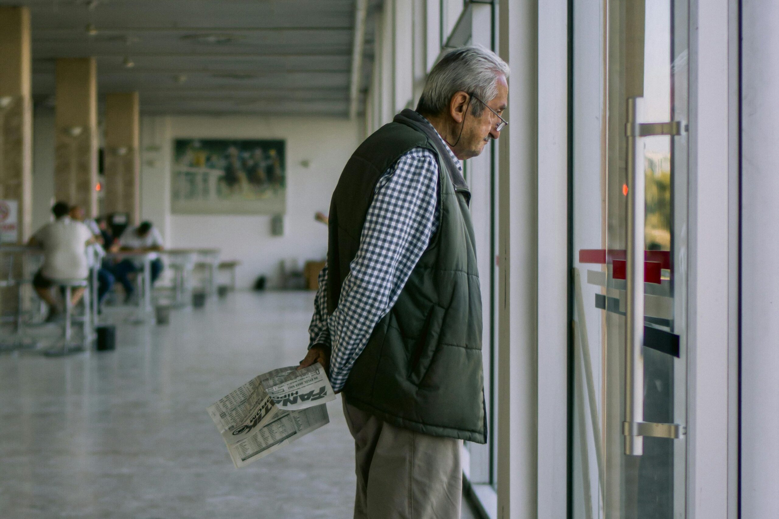 An elderly man is looking outside a big glass windows