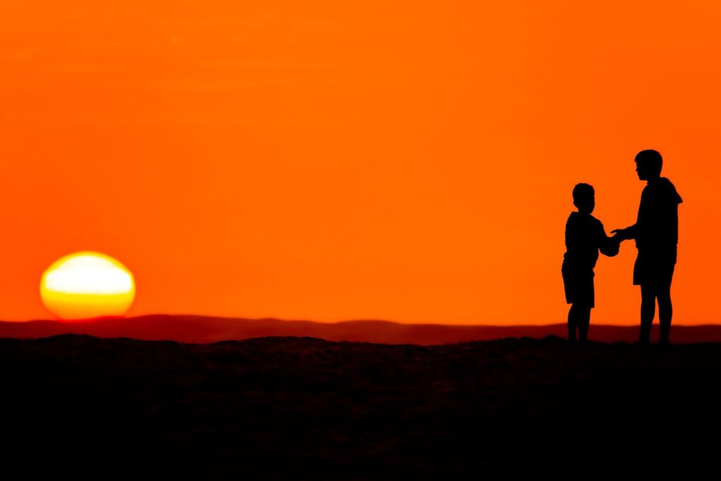 Silhouettes of two children against a sunset sky