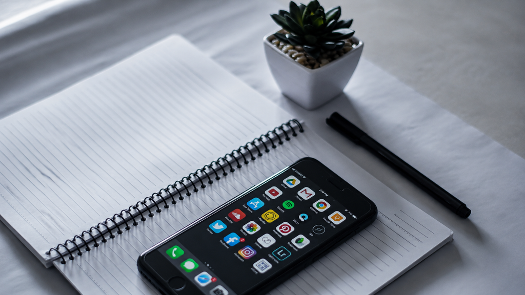 A phone with a language app on a table beside a notebook with Cyrillic handwriting
