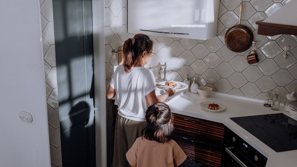 Parent cooking while a child talks to them at the kitchen table