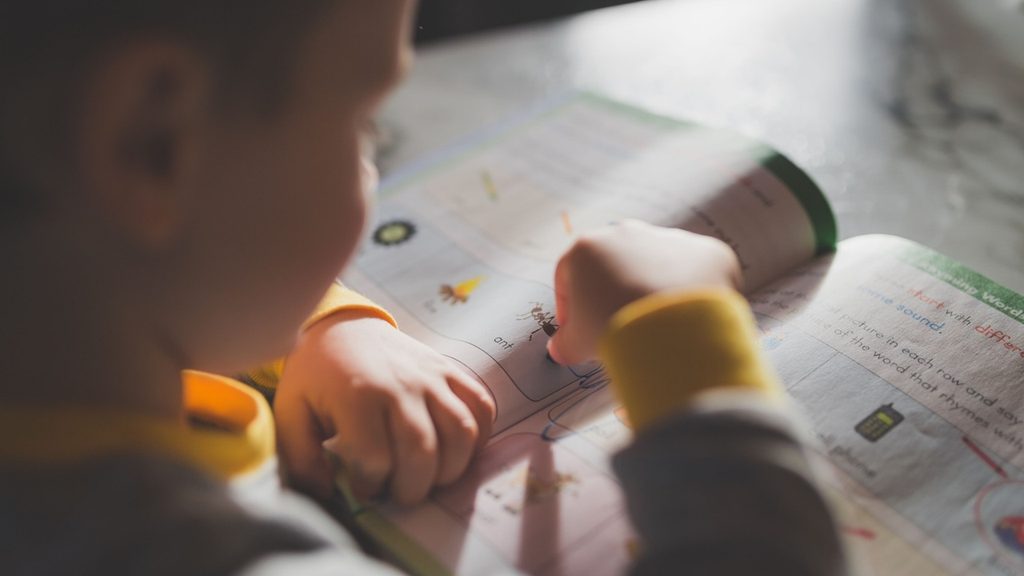 Child sitting at a table with an open notebook, looking away from the page