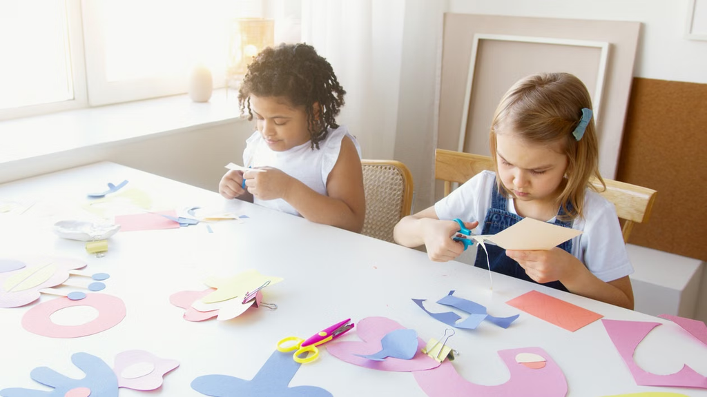 Two girls are sitting and cutting something out of paper.