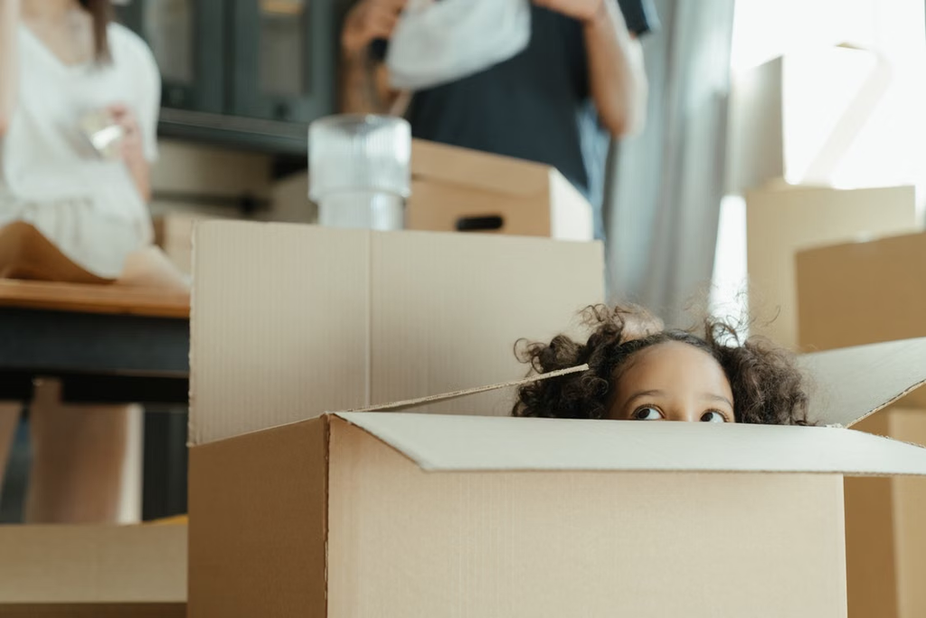A child peeks out of a cardboard box while moving to a new home, capturing a playful moment.