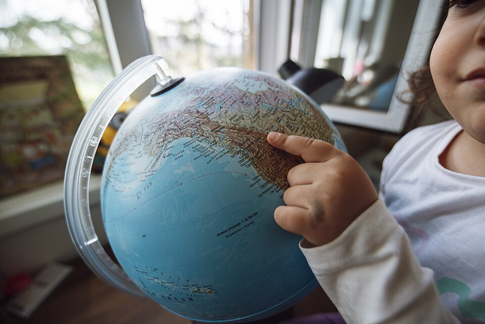 The child points to a spot on the globe at home