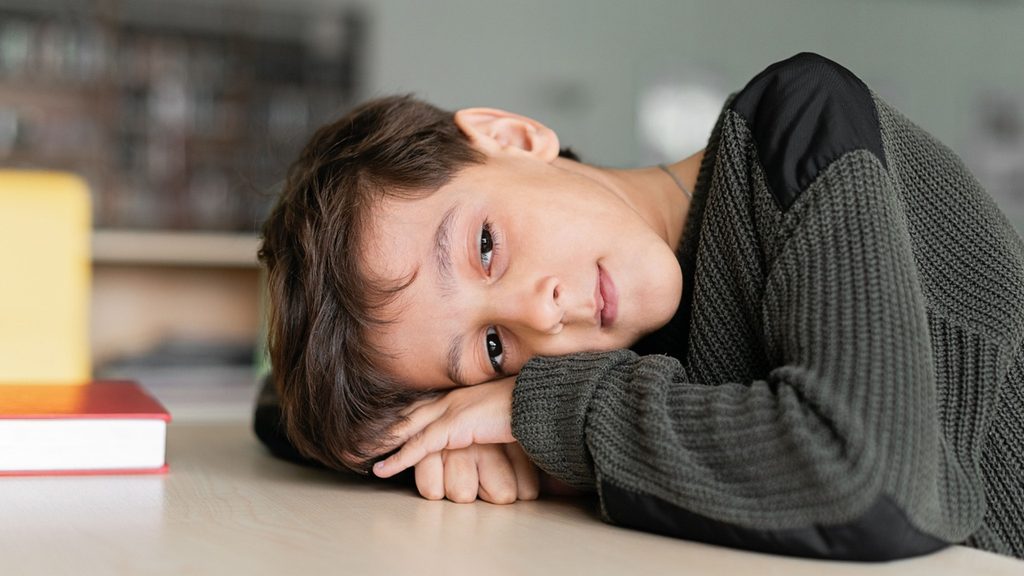 A child at a desk turned toward the window with unfinished work in front of them
