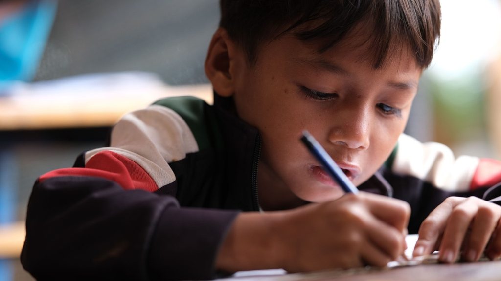 A child back at work at a table with a crumpled sheet of paper nearby