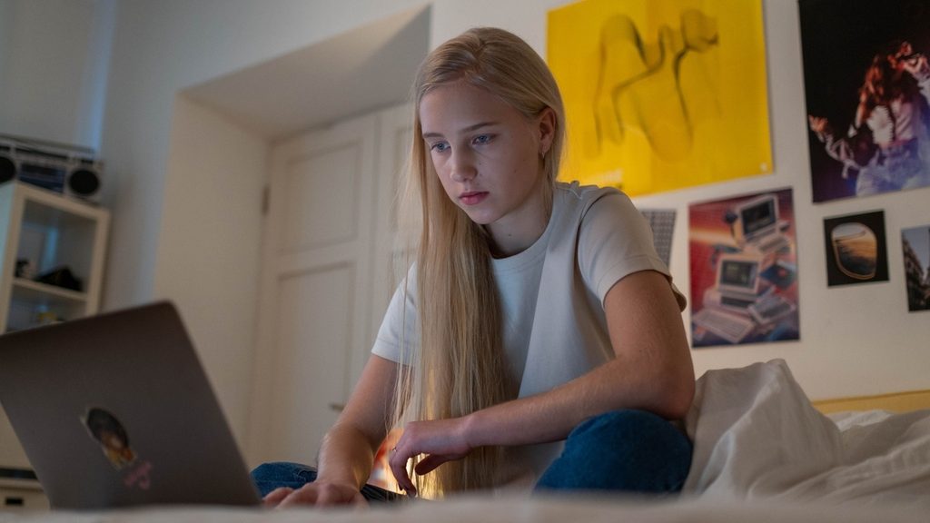 Teenager at a laptop in a shared room with other children nearby